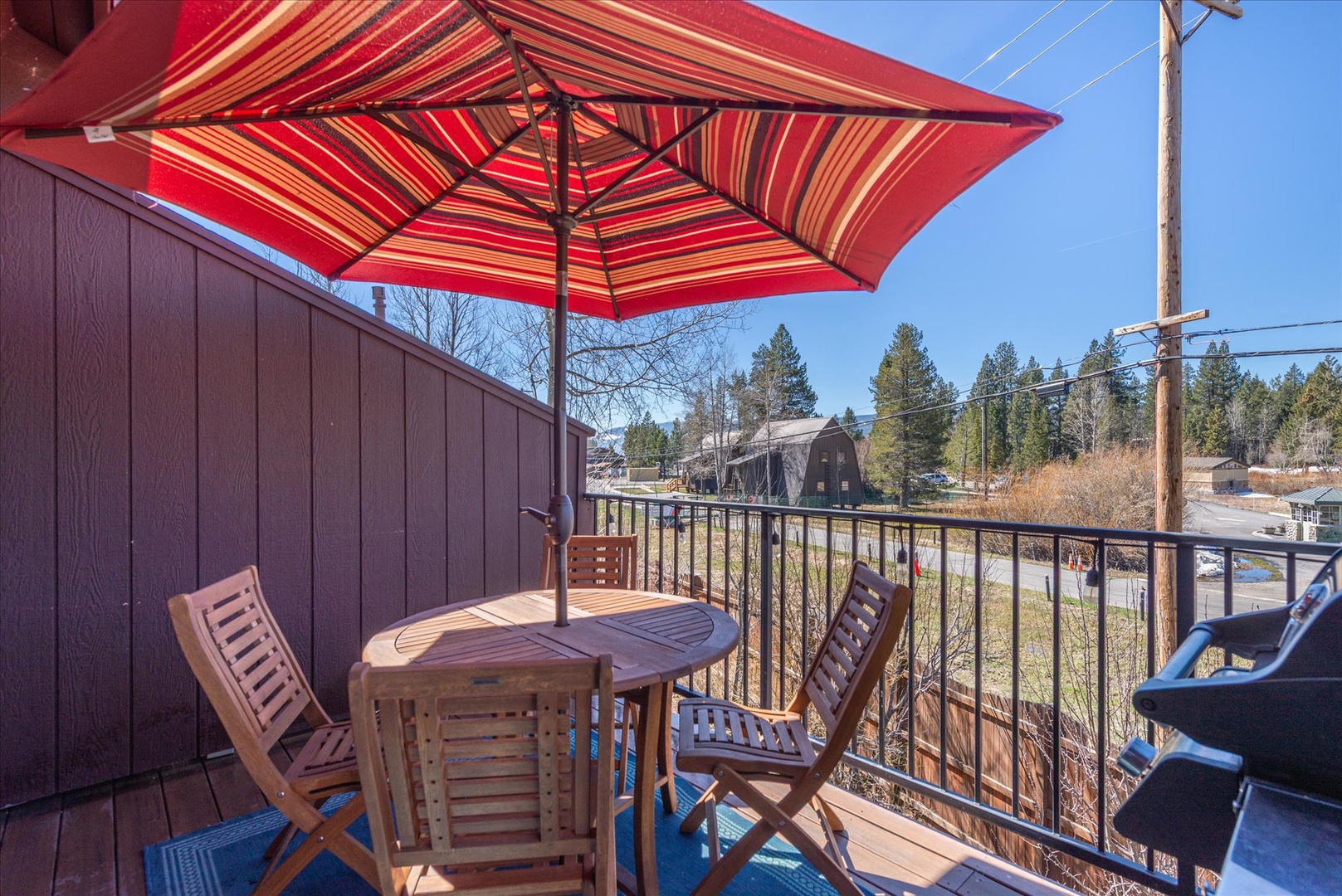 Relax on your private balcony with teak furniture and cheerful striped umbrella, overlooking peaceful meadow views.