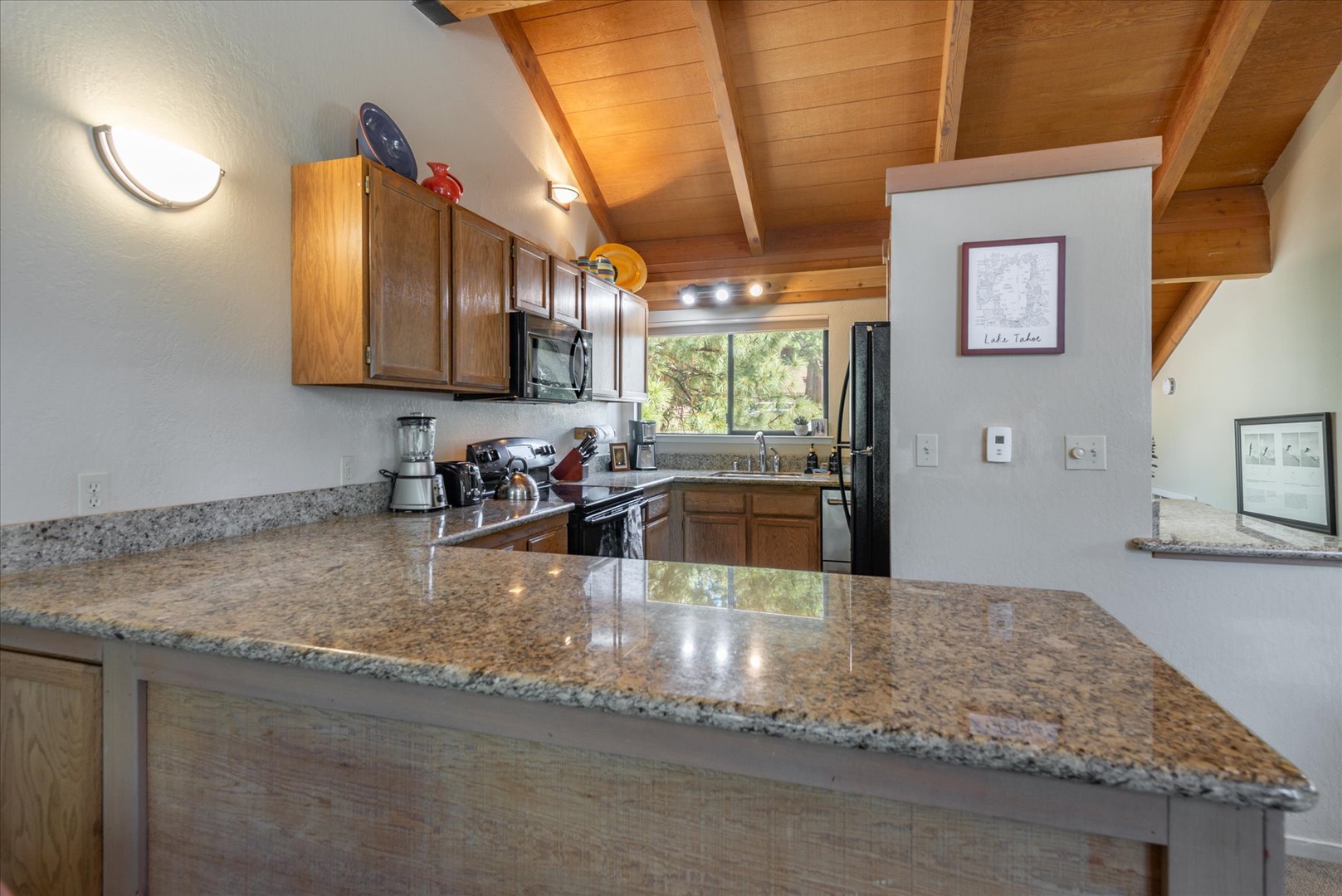 Step into your well-equipped kitchen with granite countertops, modern appliances, and warm wood accents. Sunlight streams through the window, illuminating your mountain retreat cooking space.