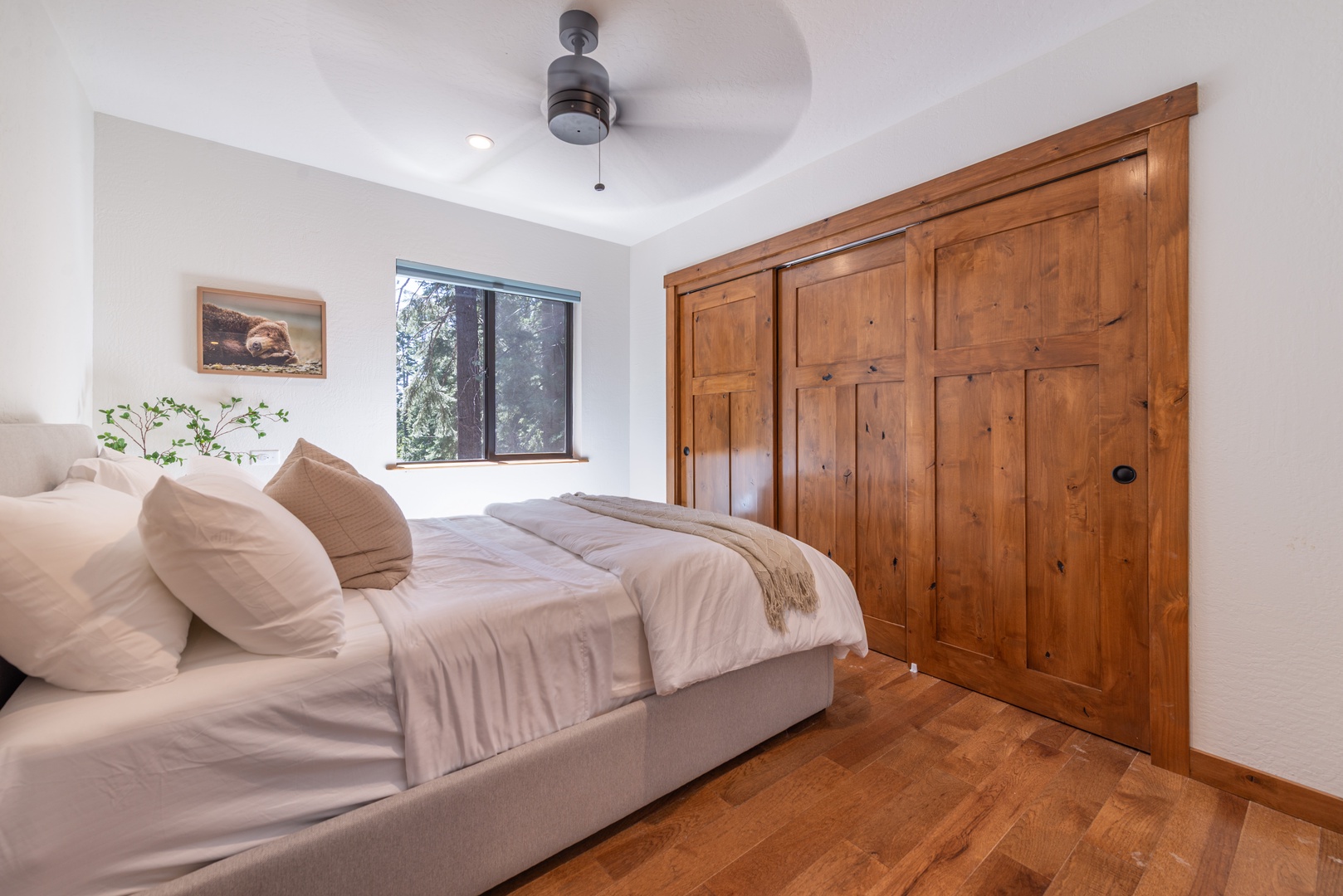 Wake up refreshed in this serene bedroom, where soft linens meet natural wood warmth. The ceiling fan keeps you comfortable, while your view of the trees sets a peaceful tone for your stay.
