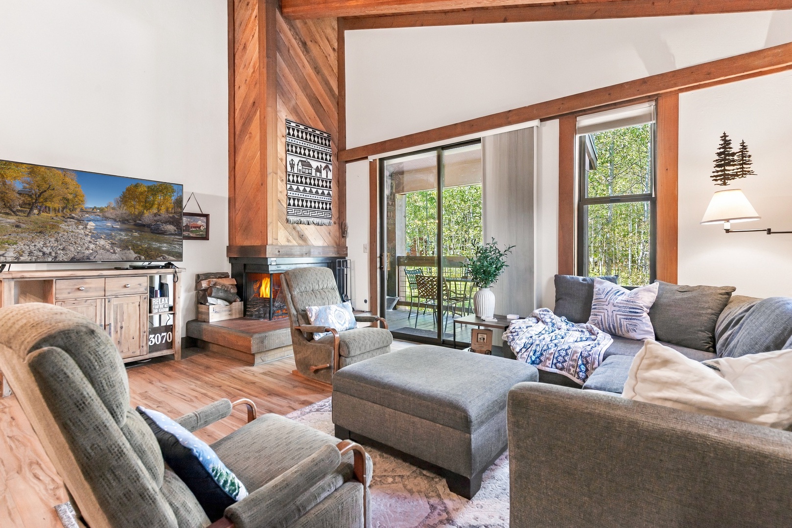 Unwind in your cozy living room with vaulted ceilings, warm wood accents, and a crackling fireplace. Large windows frame views of leafy aspens, inviting natural light and mountain-home charm.
