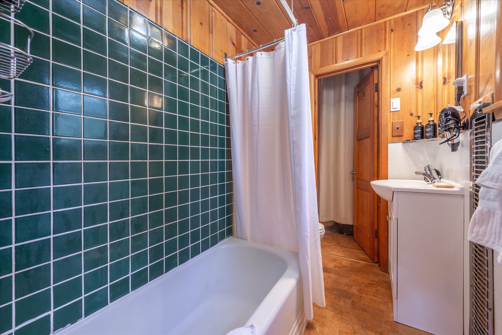 Refresh in your charming bathroom featuring beautiful green tile work, a relaxing tub, and warm wood finishes throughout.