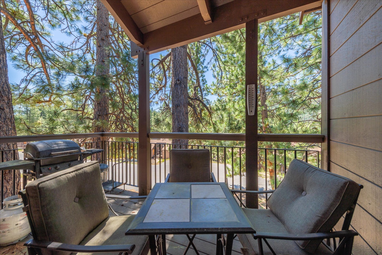 Your private covered deck invites peaceful mornings with forest views, plush seating, a table for dining outdoors, and a grill ready for your evening cookout.