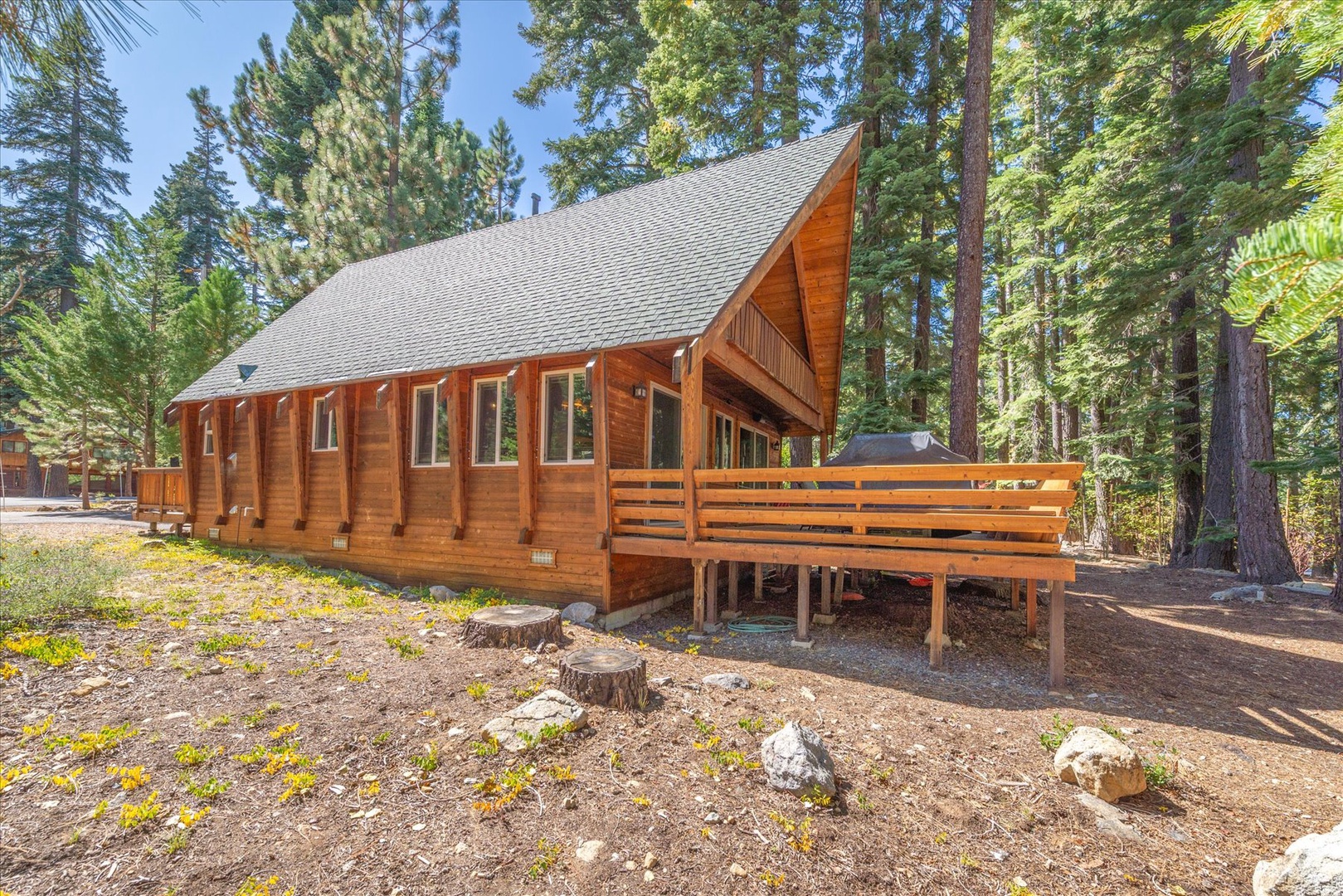 A charming wood-sided cabin nestled among towering pines and surrounded by natural landscape, featuring a spacious deck perfect for morning coffee or evening gatherings.