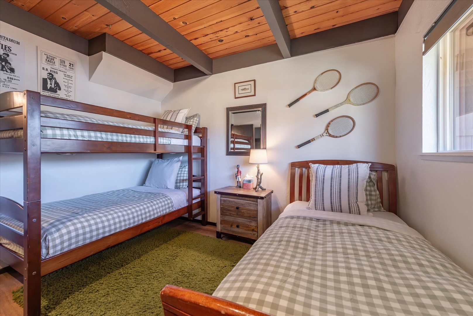 Your family's perfect retreat features comfortable bunk beds and a cozy single bed, all dressed in soft plaid linens under rustic wood beam ceilings.