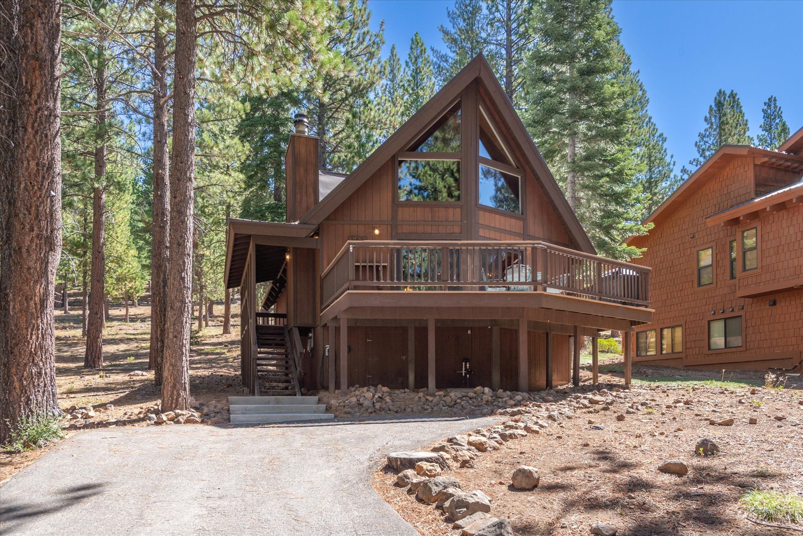 A classic A-frame cabin nestled among towering pines, featuring a welcoming deck and mountain charm in a peaceful forest setting.