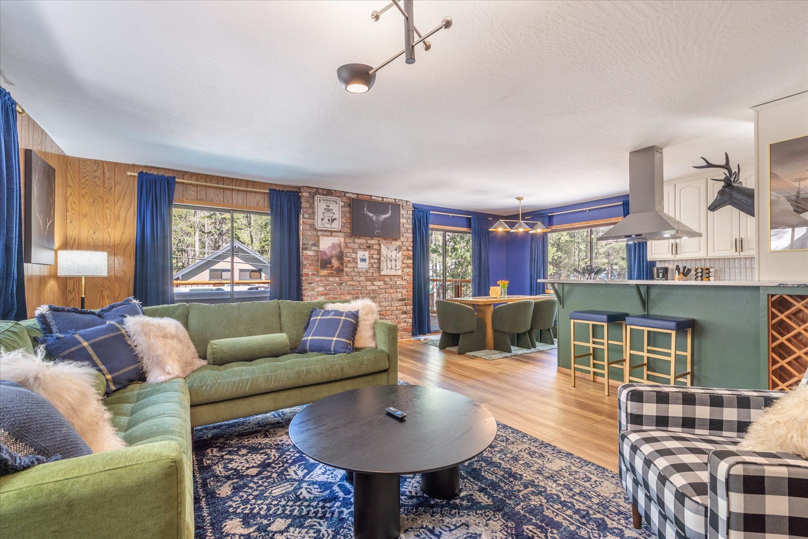 Unwind in your spacious living area featuring plush green sofas and a striking brick accent wall, perfectly connected to the modern kitchen.