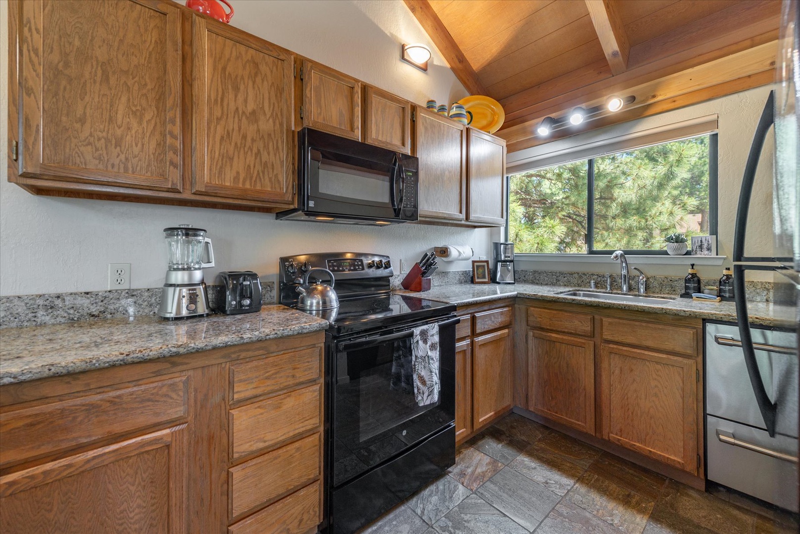 Your spacious kitchen features granite countertops, modern appliances, and warm wood cabinetry with a large window framing lush mountain views—perfect for enjoying morning coffee as you cook.
