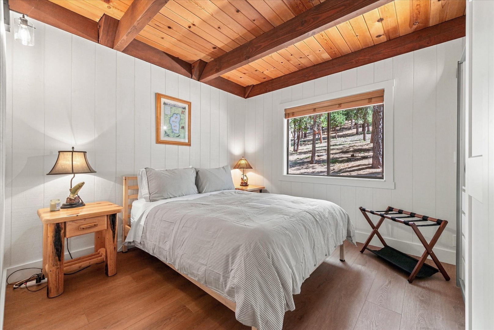 Wake up to warm wood tones and natural light streaming through your window, revealing peaceful forest views. This cozy downstairs bedroom wraps you in rustic charm with its exposed beams and inviting linens.