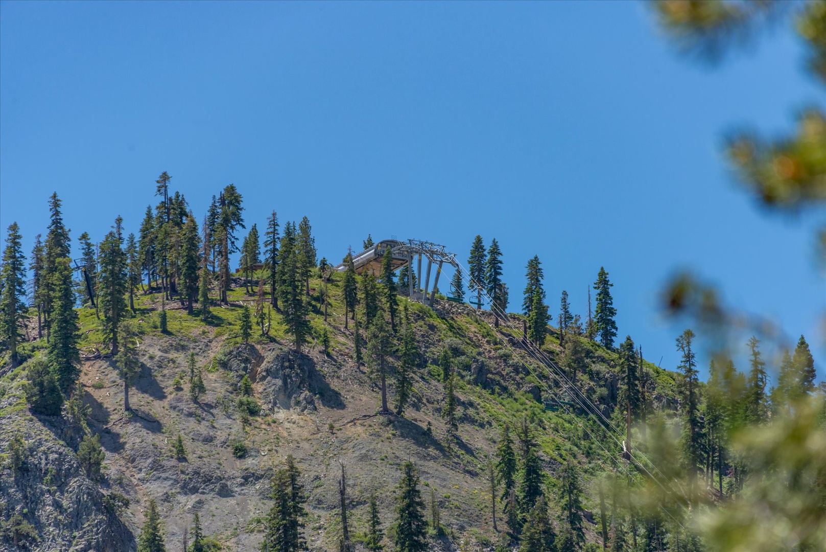 A scenic mountainside covered with evergreen trees features a chairlift system, indicating nearby ski facilities. The clear blue sky and natural landscape showcase the property's alpine setting.