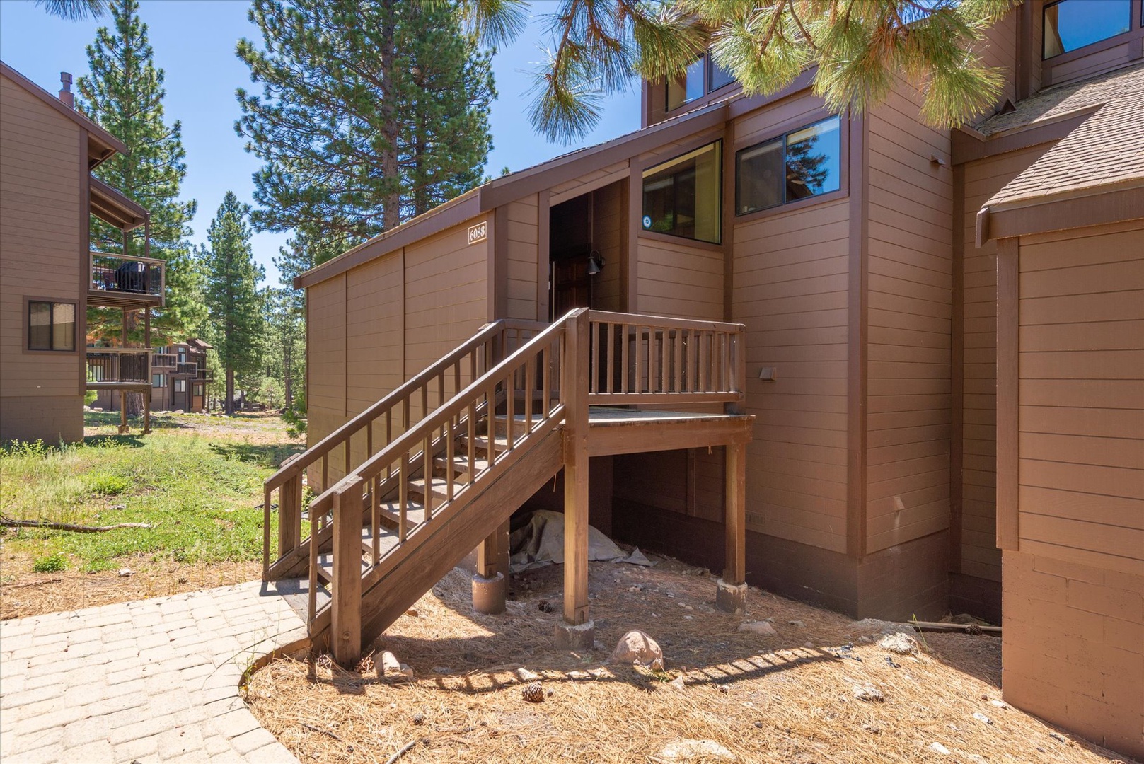 This mountain retreat features a private entrance with rustic wood siding and a sturdy wooden staircase, nestled among tall pines in a peaceful alpine neighborhood.