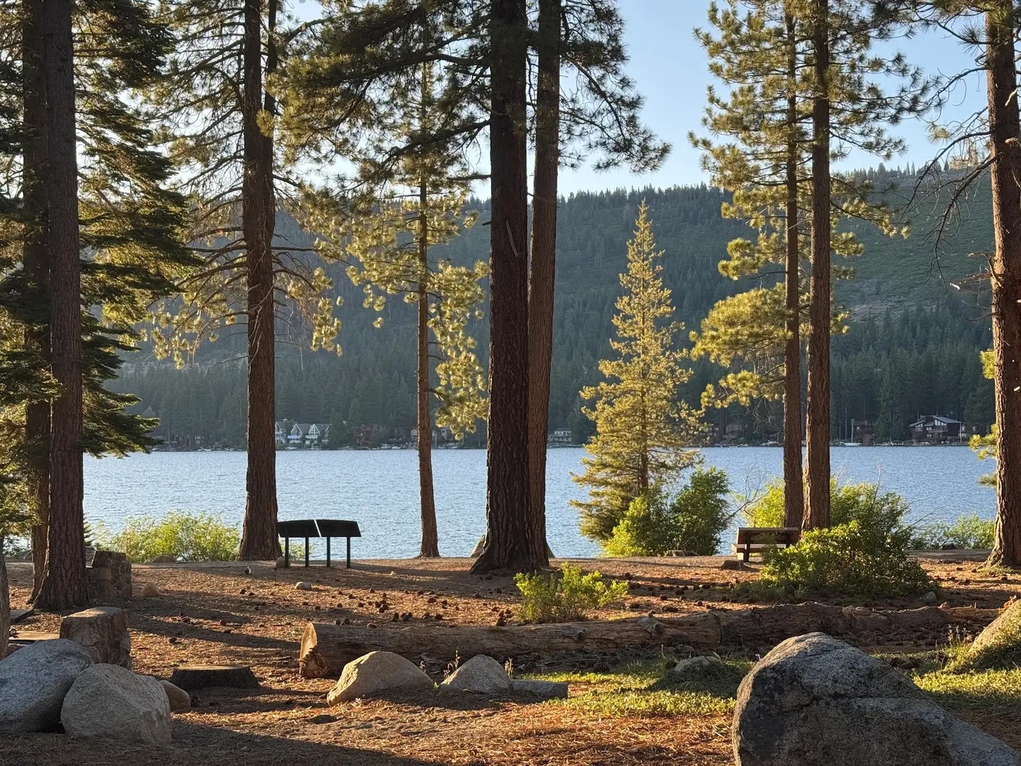 Donner Lake is set with towering pines, scattered boulders, and picnic tables overlooking calm waters and forested mountains.