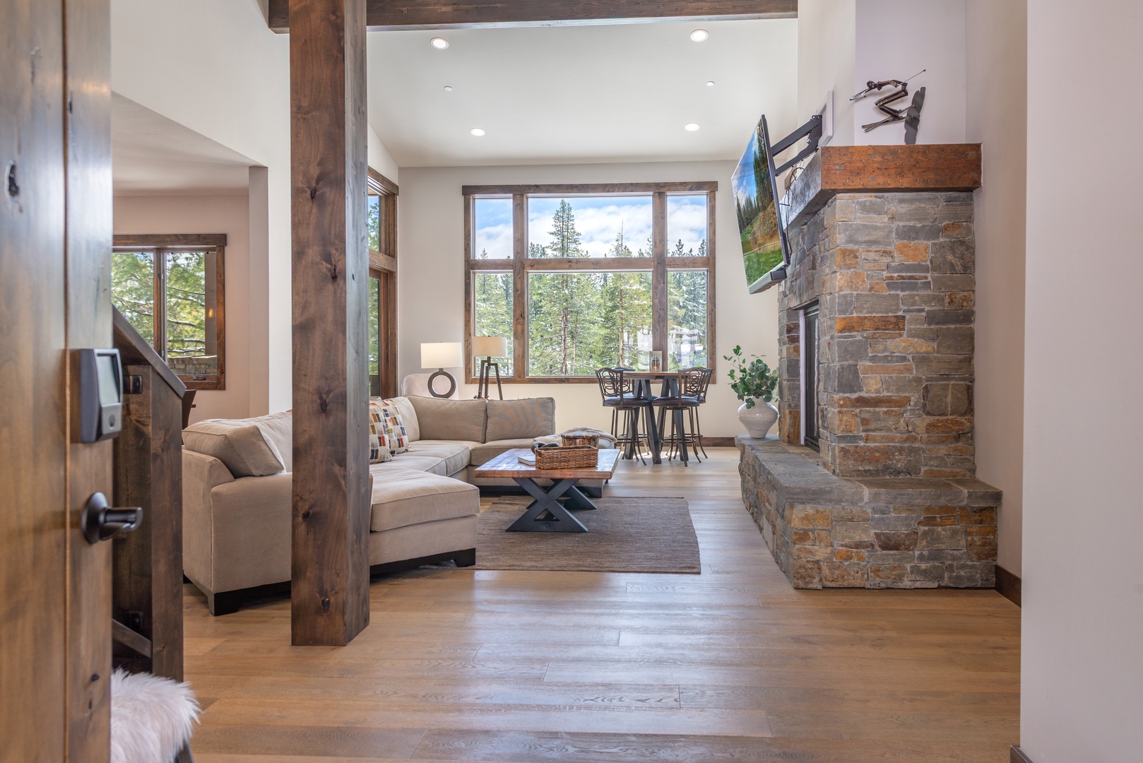 Unwind in your stylish living room featuring a stone fireplace, cozy sectional, and stunning forest views through expansive windows.