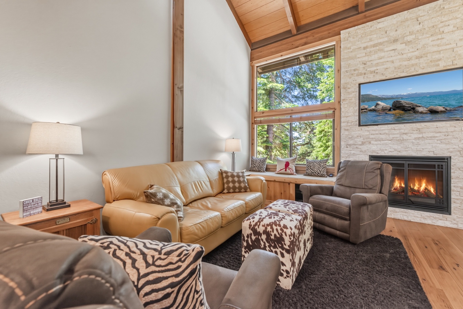 Relax in your inviting living room with vaulted wood ceilings, a cozy fireplace, and plush seating that frames stunning lake views through tall windows.