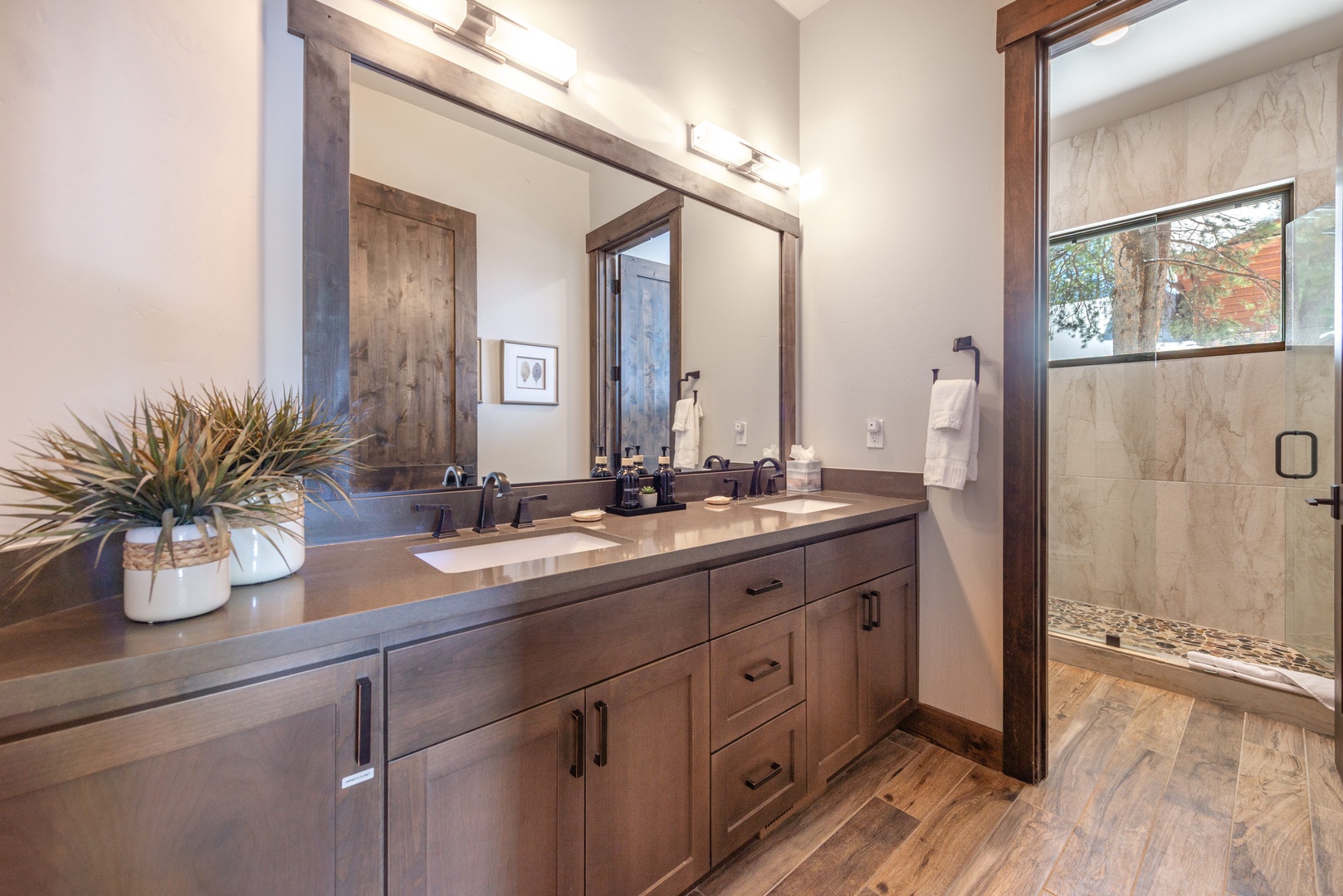 Unwind in your spacious bathroom with warm wood finishes, dual vanities, and a glass-enclosed shower featuring natural stone accents.