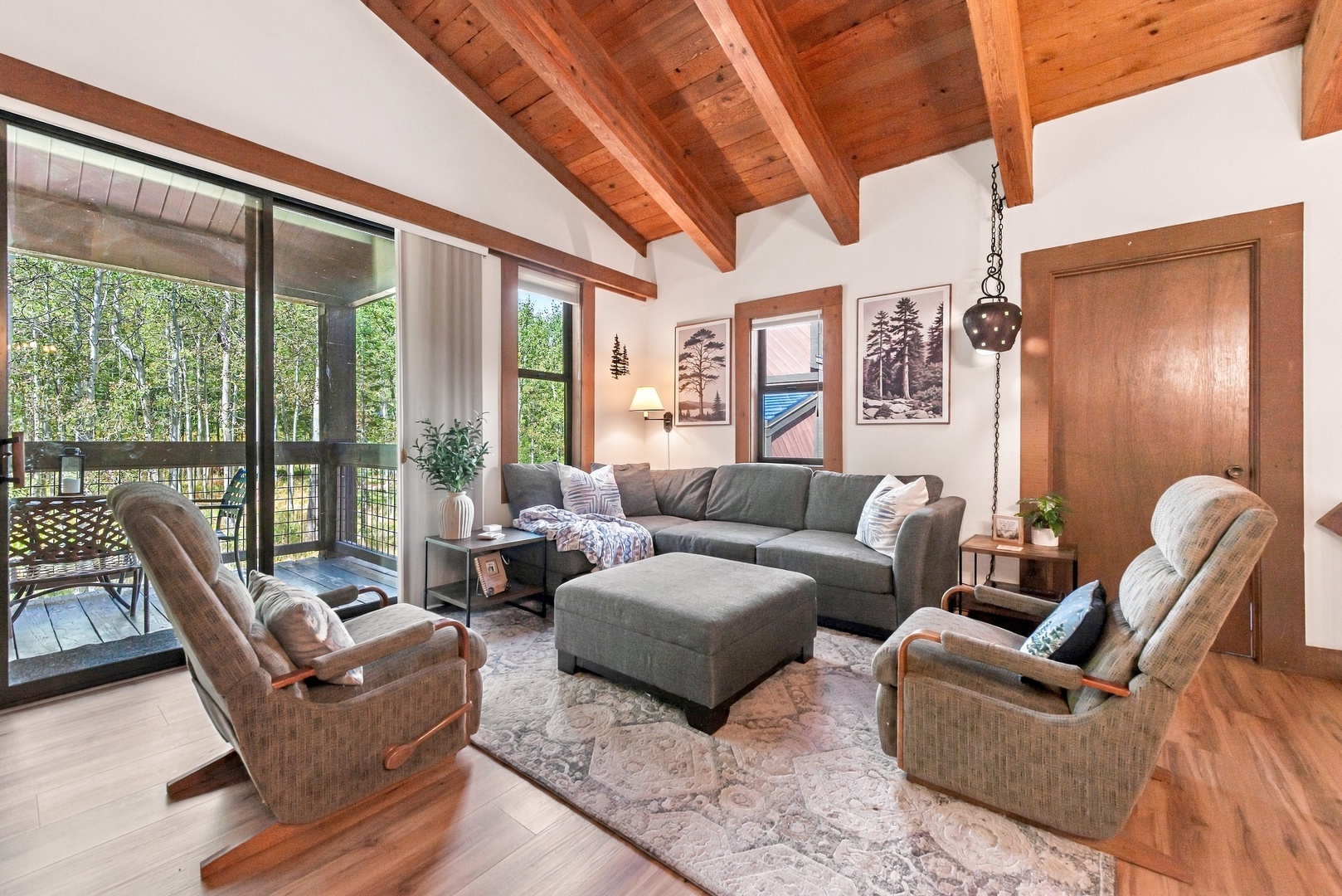 Unwind under soaring wood-beam ceilings in your cozy living room, where plush seating invites relaxation and natural light pours in from forest views just beyond the glass doors.