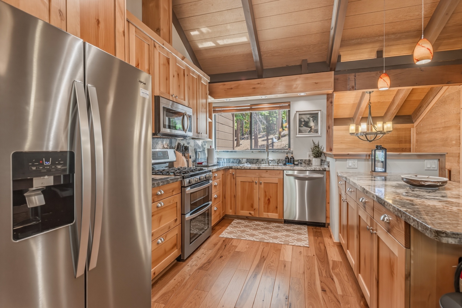 Step into a chef-ready kitchen where natural wood meets modern appliances. Granite counters and stainless steel appliances shine under vaulted ceilings, while forest views through the window inspire your next meal.