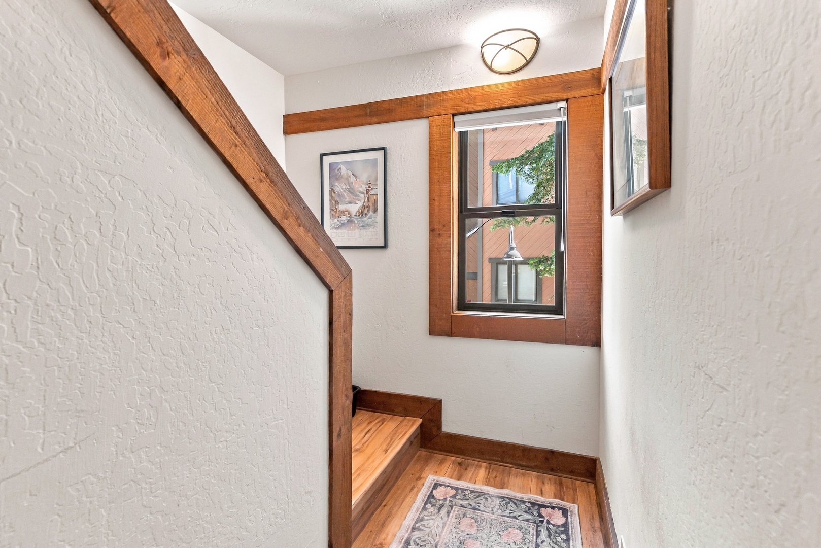 A cozy stairwell landing greets you with warm wood accents and natural light streaming through the window. The charming hardwood details and crisp white walls create an inviting atmosphere as you move through your mountain retreat.