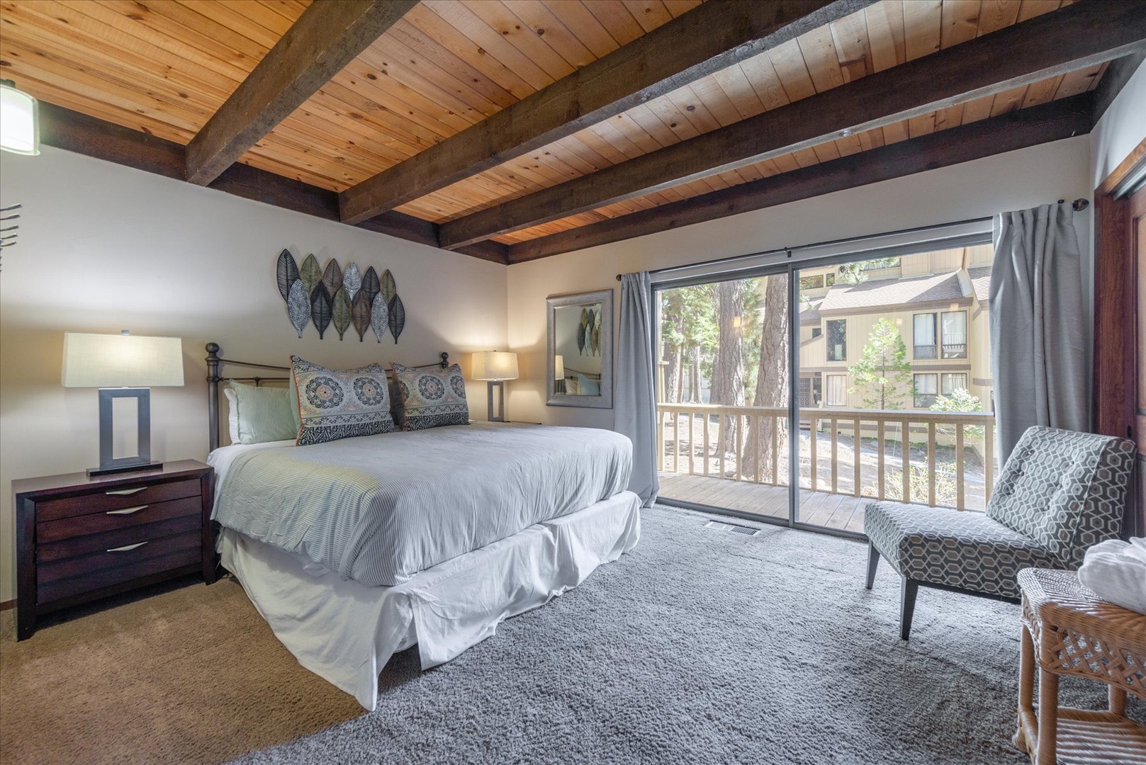 Unwind in your spacious master bedroom with exposed wood beams, plush bedding, and peaceful balcony views of surrounding trees.