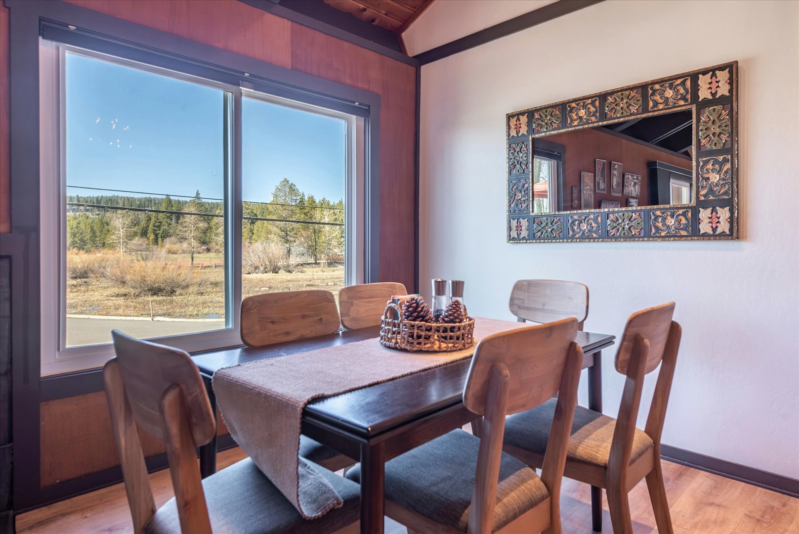 Gather around your rustic dining table where warm wood meets artistic charm, with nature's beauty framed perfectly outside your window.