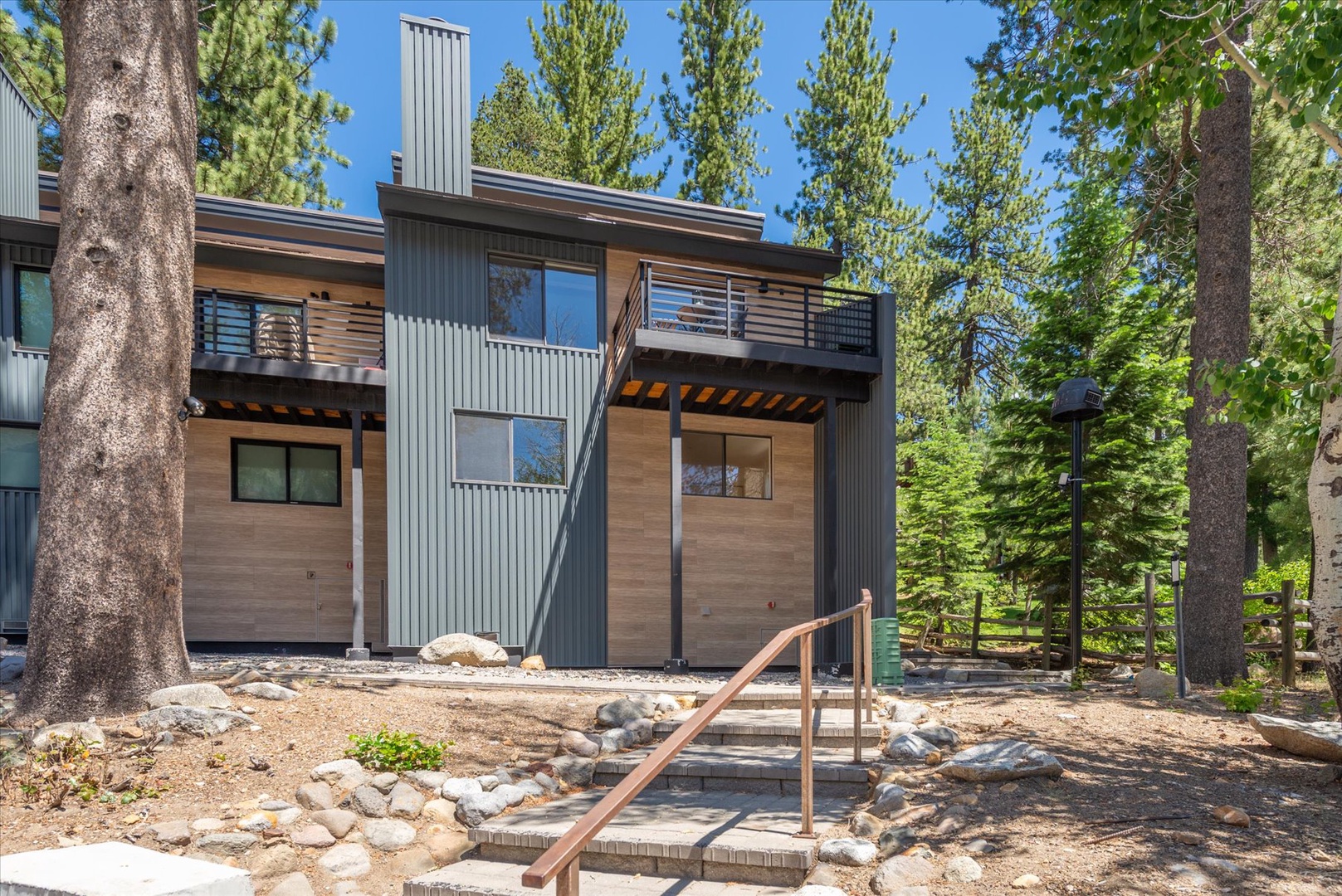 Modern mountain retreat nestled among towering pines, featuring natural wood and metal siding with a private balcony perfect for enjoying the fresh alpine air.