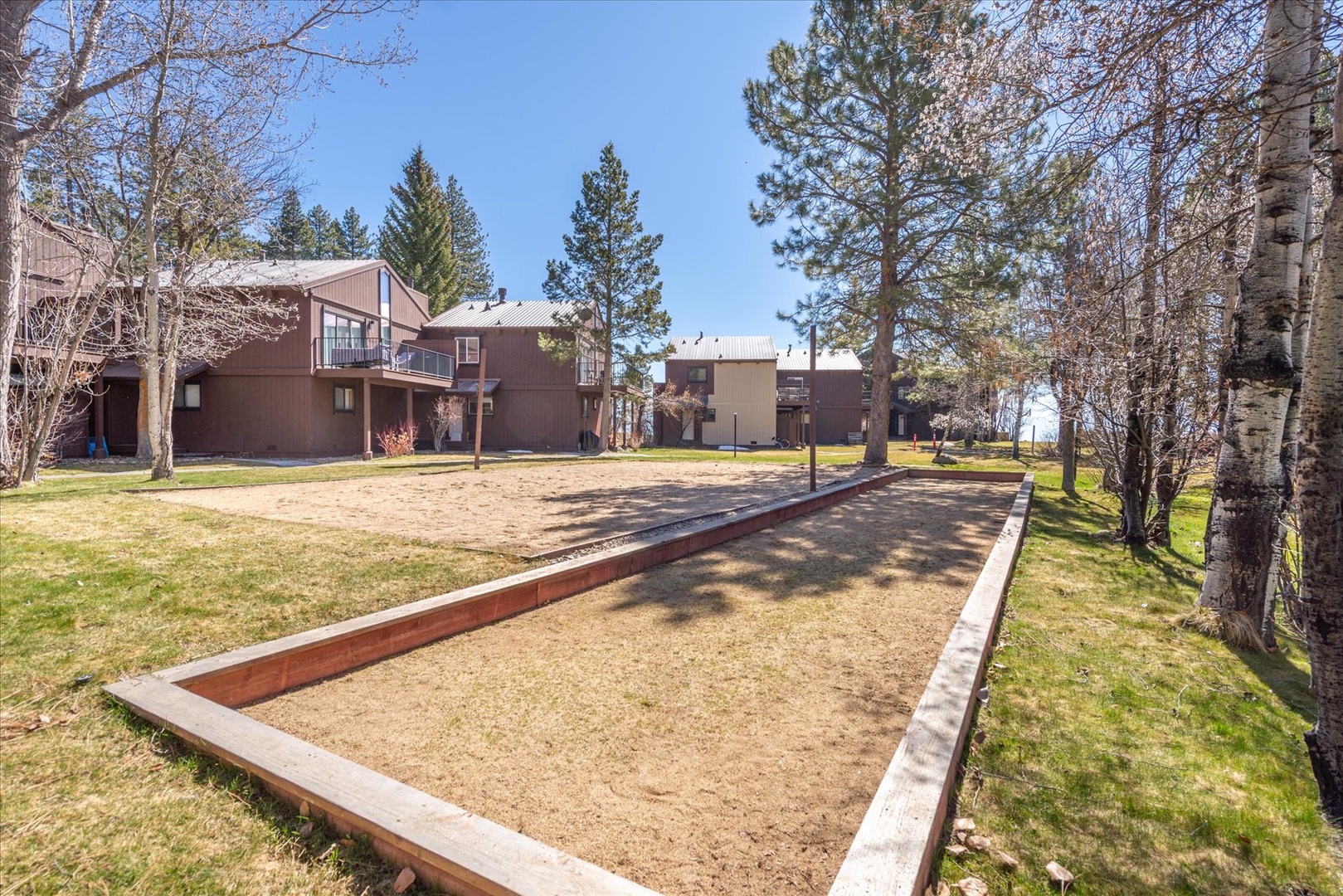 Property features outdoor recreational area with bocce ball court surrounded by mature trees and mountain forest setting.