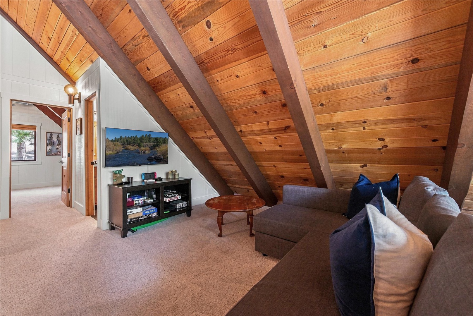 Relax under soaring wood-beamed ceilings in your cozy loft living space, complete with comfortable seating and serene lake views displayed for your enjoyment.