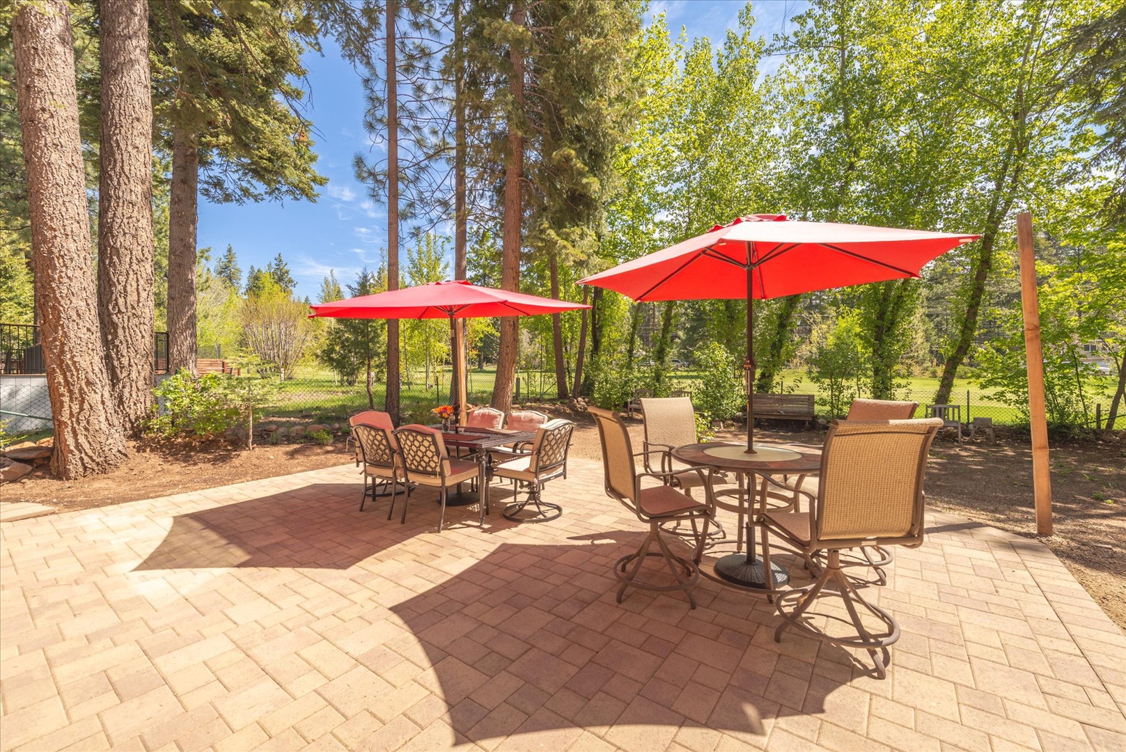 Your private patio awaits with comfortable dining sets under vibrant red umbrellas, perfectly positioned for memorable meals surrounded by towering pines.