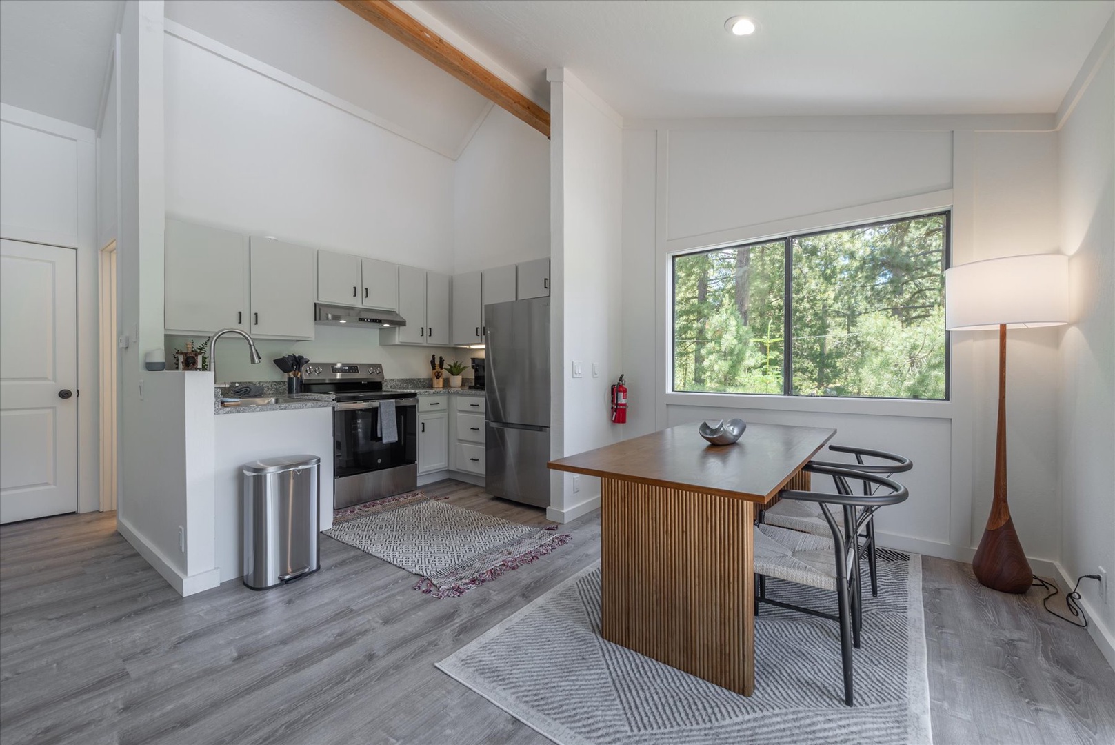 Your bright, modern kitchen features sleek appliances, warm wood accents, and abundant natural light—perfect for preparing meals while enjoying peaceful tree-lined views through the large window.