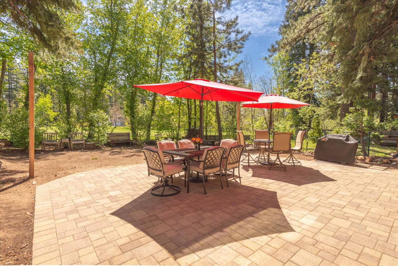 Relax on your private paved patio surrounded by towering trees, with comfortable dining seating under vibrant red umbrellas for perfect outdoor entertaining.