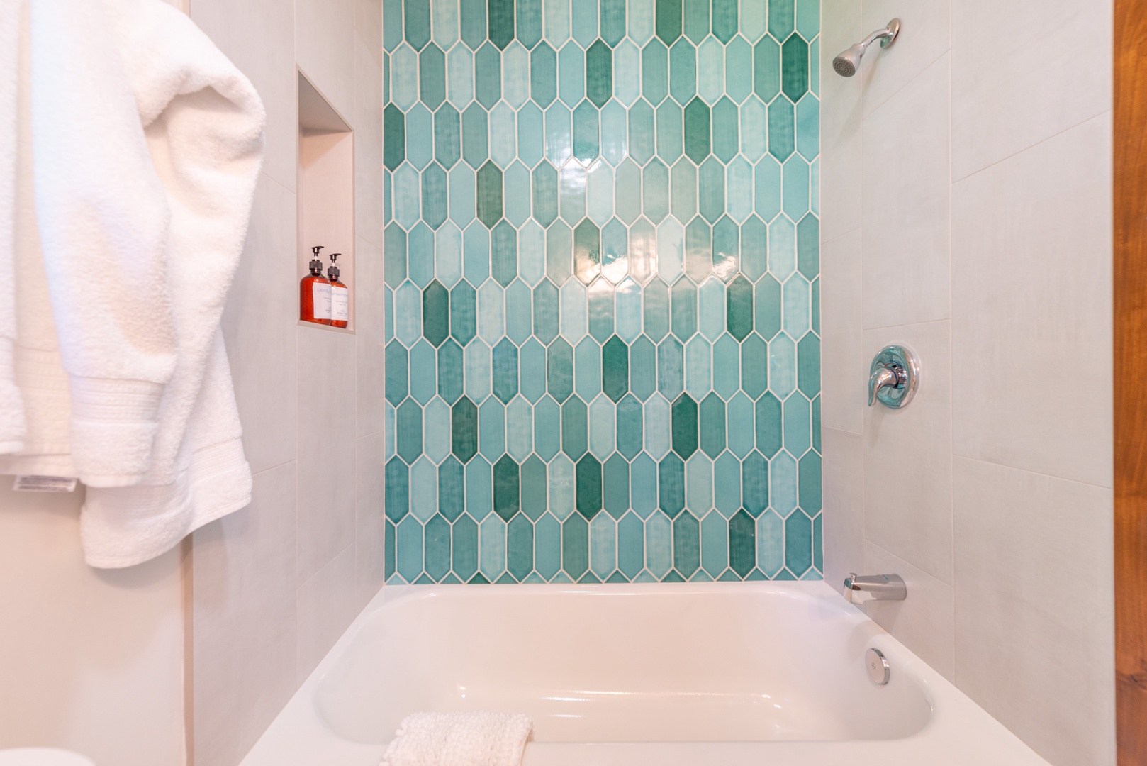 Unwind in your elegant bathroom featuring stunning seafoam geometric tile work and shower tub, perfect for relaxing after your adventures. Provided amenities await your arrival.