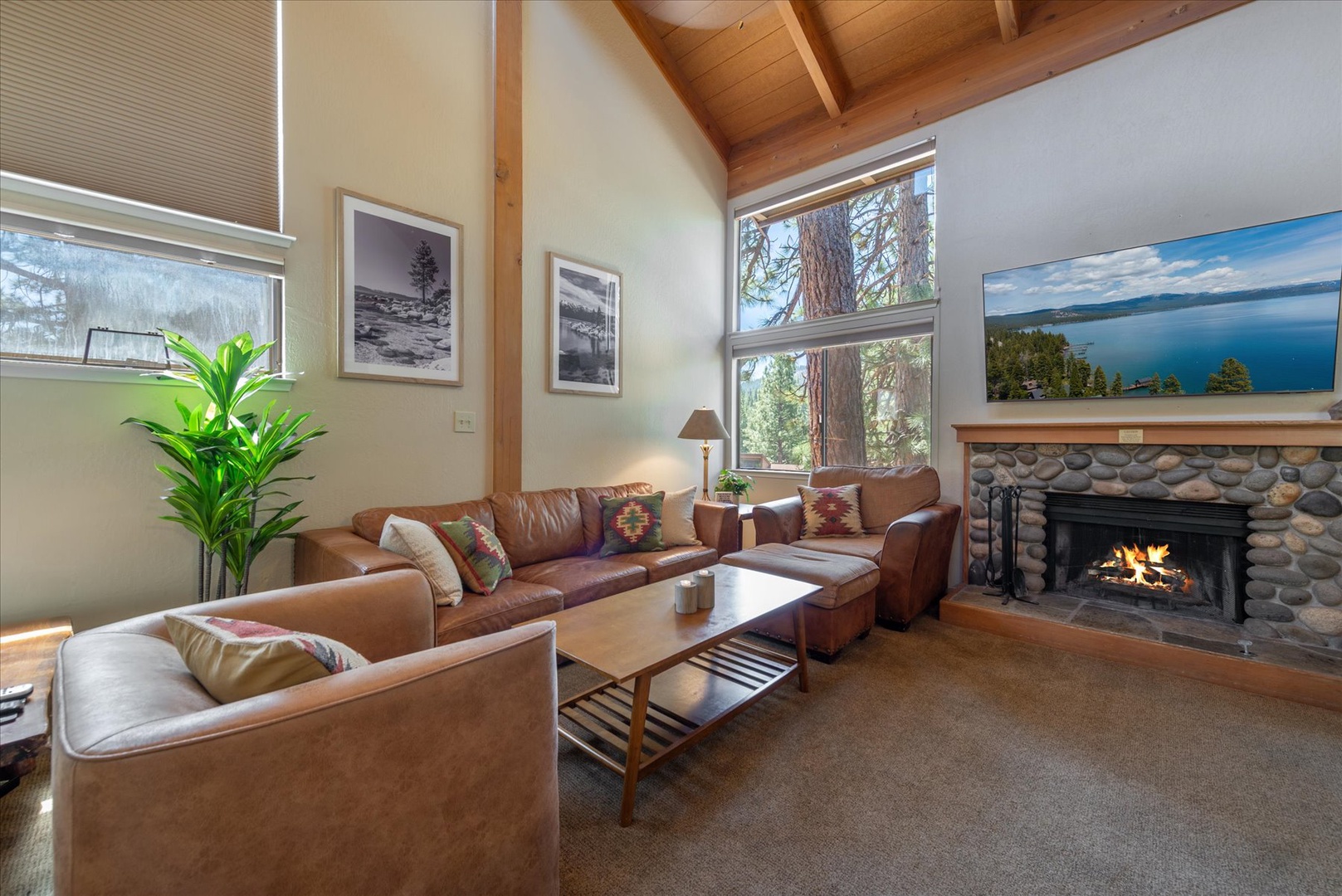 Sink into plush leather sofas by the crackling fireplace as towering pines frame your mountain retreat, where vaulted wood ceilings and natural light create your perfect sanctuary.