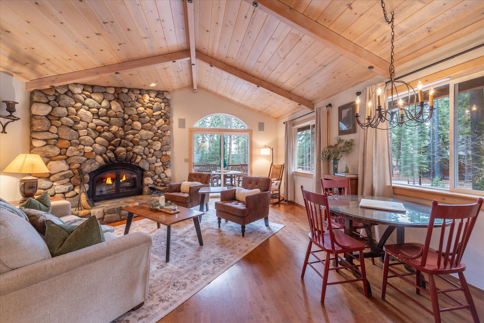 This spacious living room, with a cozy sitting area and game table, is framed by the vaulted ceilings and forest views.