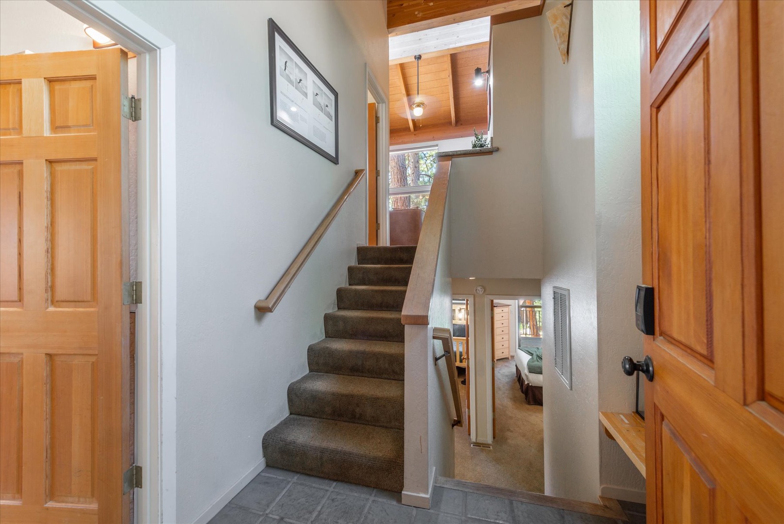 A warm entryway welcomes you with carpeted stairs leading to cozy living spaces above, finished with handsome wood accents and vaulted ceilings that create an airy mountain retreat atmosphere.