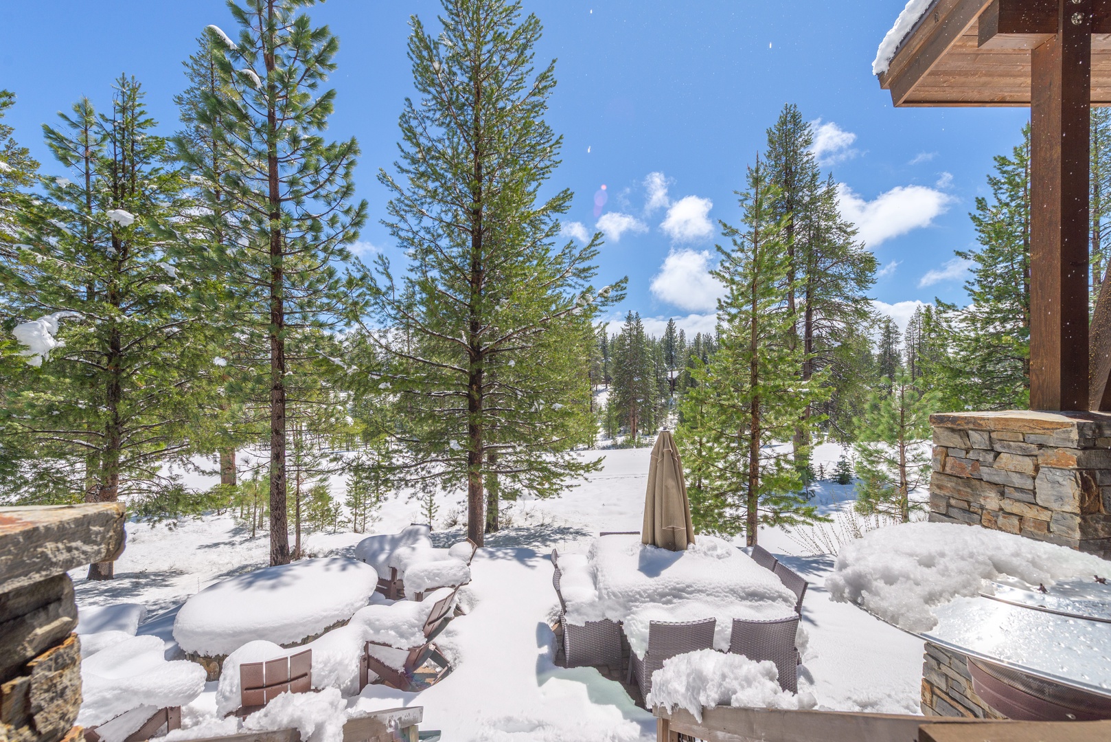 Snowy mountain property featuring outdoor seating areas surrounded by pristine winter forest under bright blue skies.