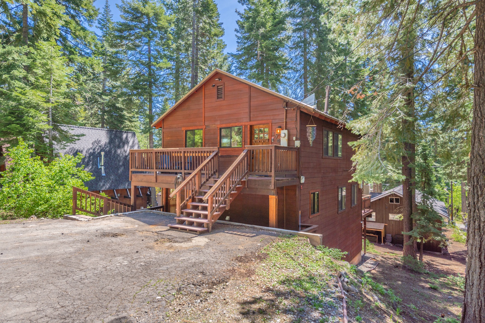 A charming mountain cabin nestled among towering pines, featuring warm wood siding, a spacious deck, and plenty of parking—your perfect forest getaway awaits.