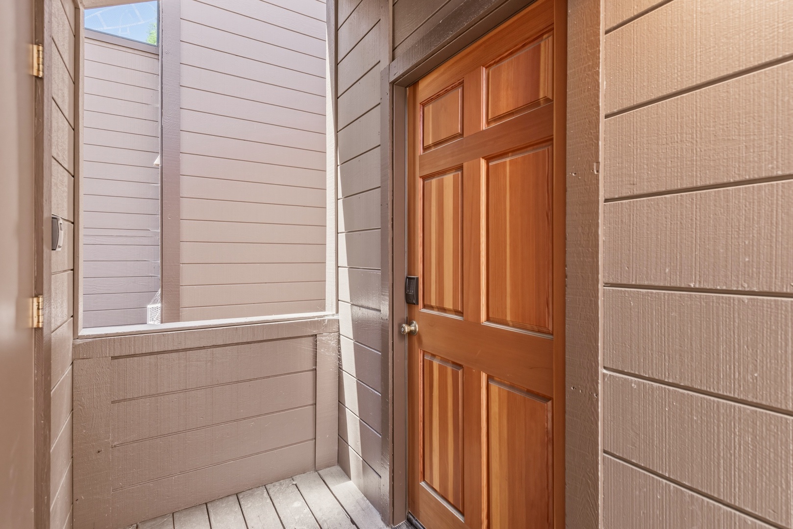 A warm wooden door welcomes guests at the property entrance, with neutral siding framing a simple yet inviting arrival point.