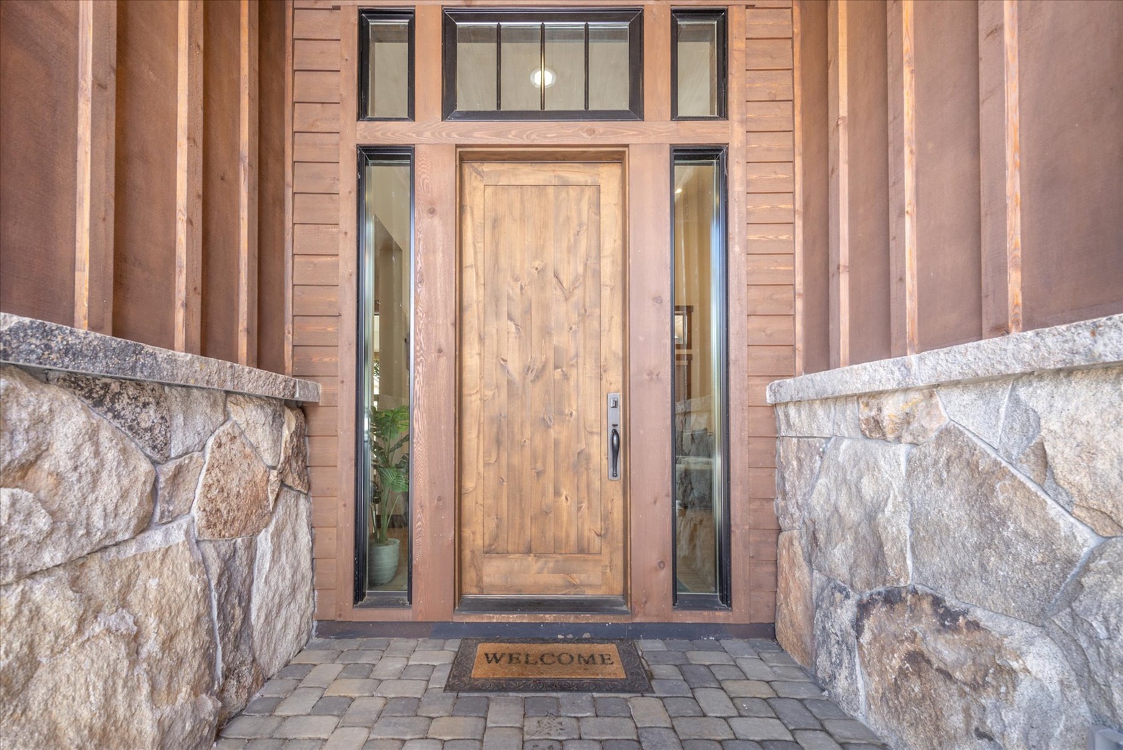 Grand stone and wood entrance with welcoming mat and architectural columns creates an impressive arrival experience.