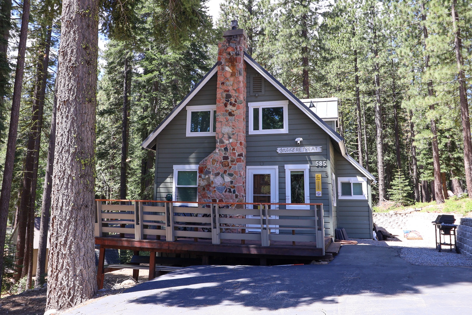 A charming A-frame cabin nestled among towering pines, featuring a striking stone chimney and welcoming front deck. The secluded forest setting offers a peaceful mountain retreat surrounded by nature's beauty.
