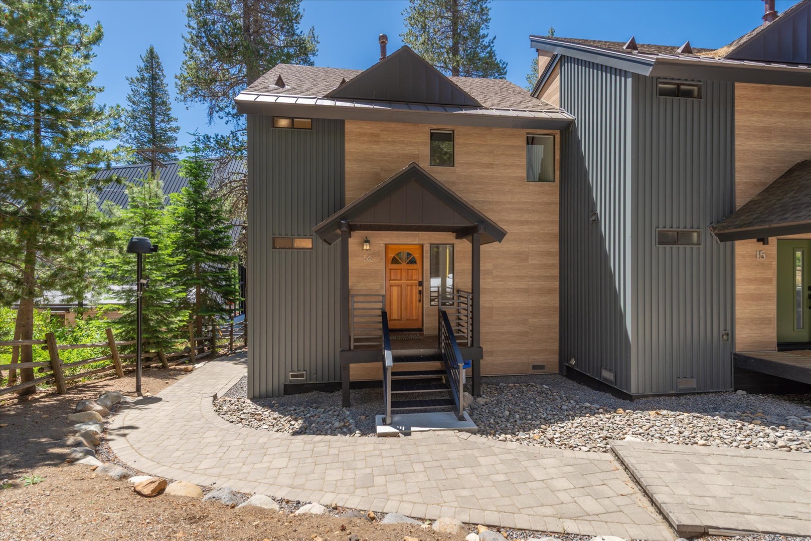 Modern mountain retreat with warm wood and metal exterior, nestled among towering pines. The welcoming front entrance and paved walkway mark the start of your alpine getaway.