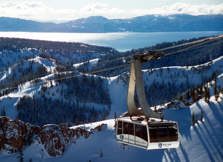 Aerial tram ascending above snow-covered mountain slopes with expansive lake views and distant peaks in the background.