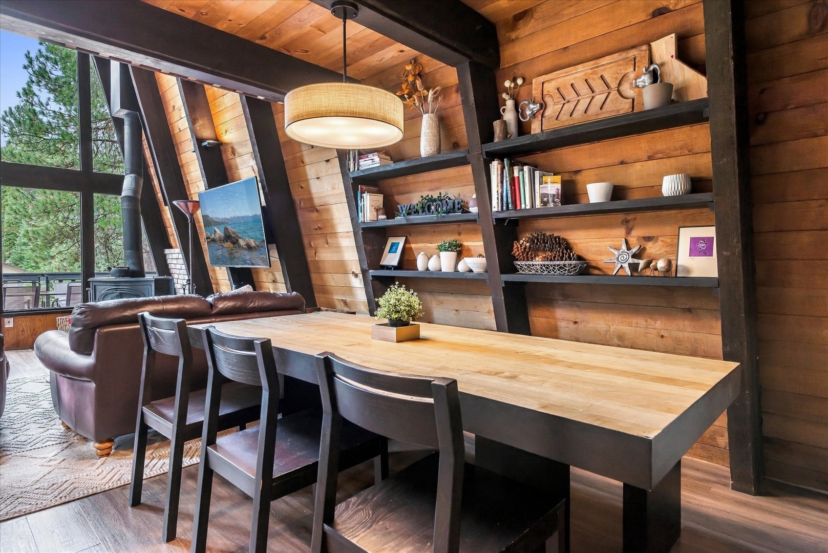 Gather around your farmhouse dining table surrounded by warm wood walls and natural light streaming through expansive windows. Shelving displays curated decor pieces that make this inviting space feel like home.