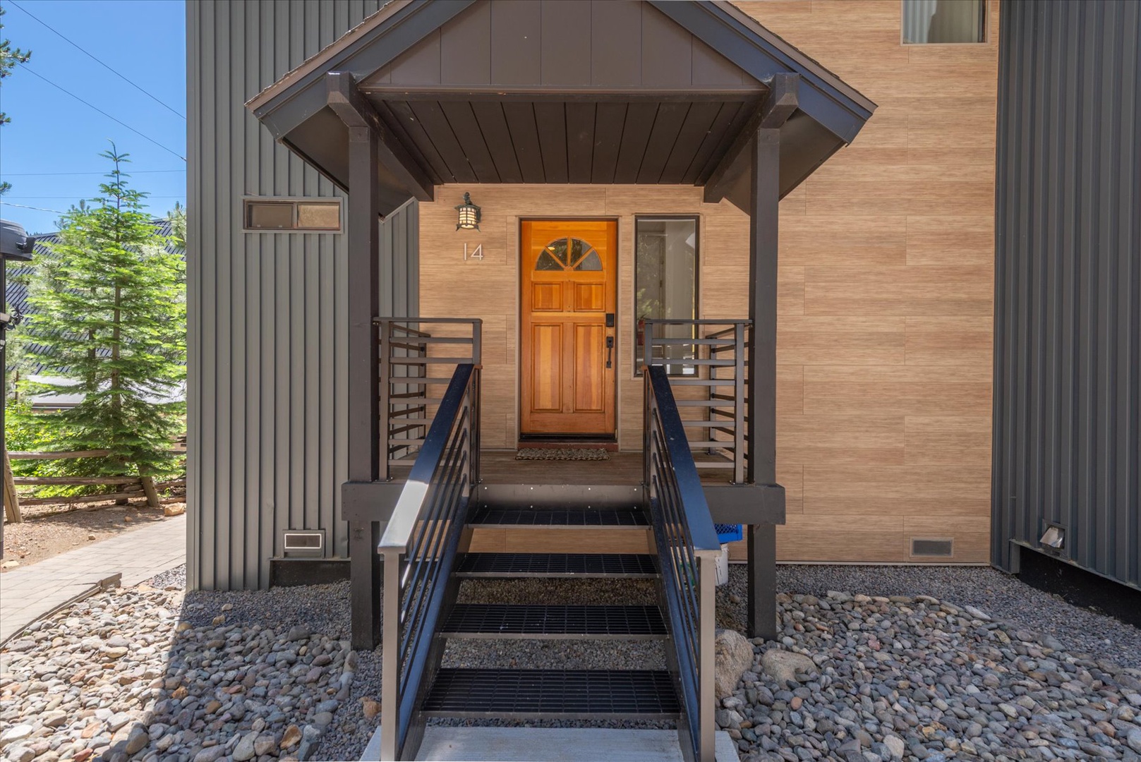 Modern mountain retreat entrance with warm wood tones and covered porch, nestled among evergreen trees in a quiet residential setting.