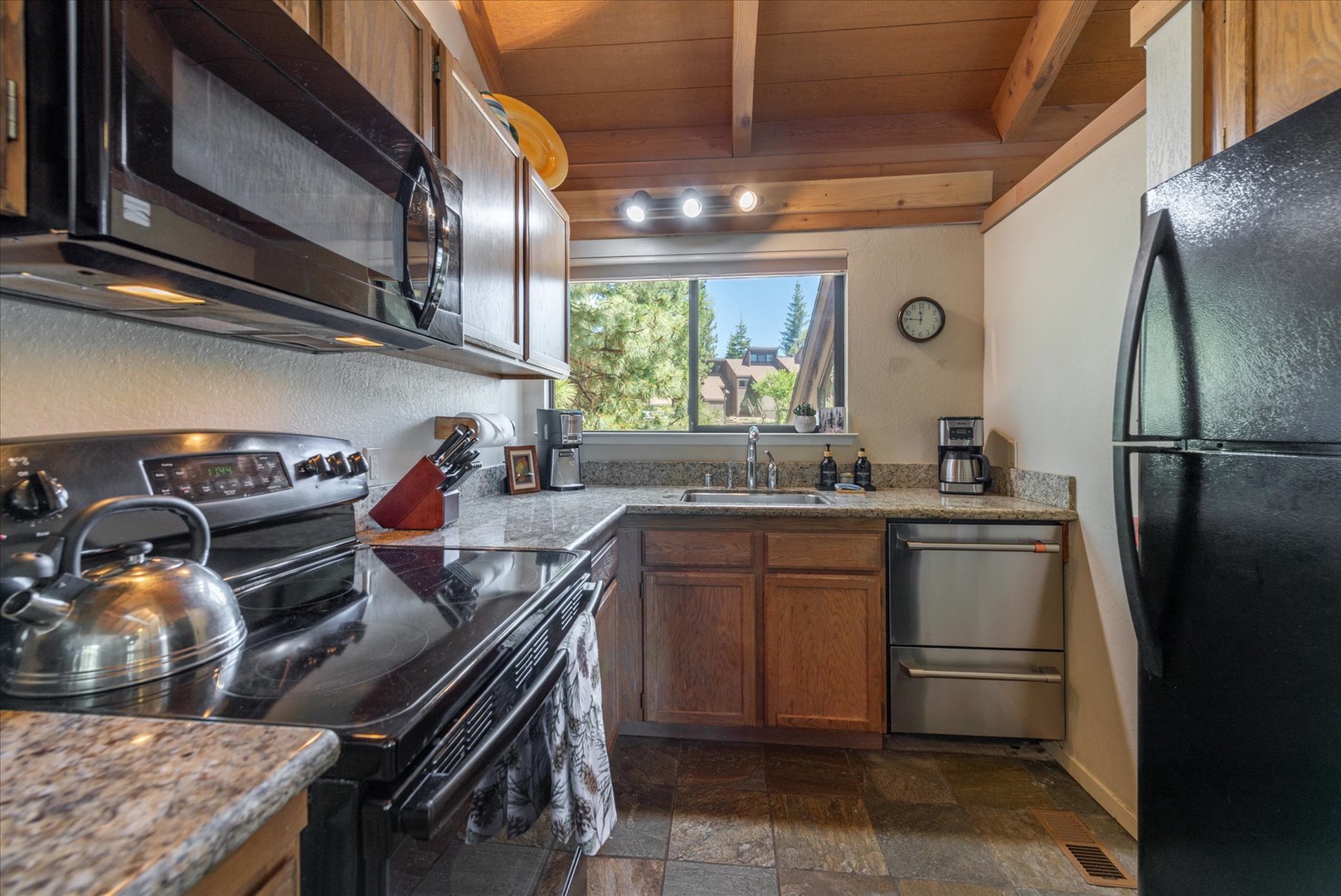 Your fully equipped kitchen features stainless appliances, granite counters, and warm wood cabinetry beneath vaulted ceilings—everything you need to prepare meals while soaking in natural light and mountain views.