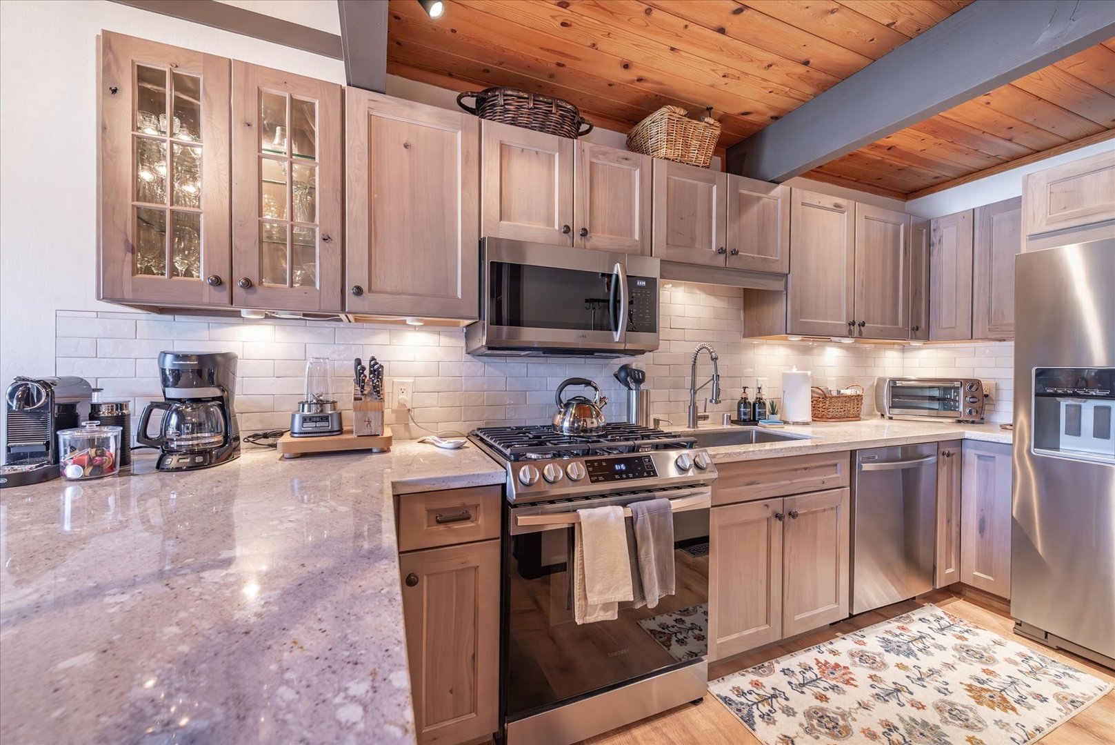 Your gourmet kitchen awaits with marble countertops, stainless appliances, and warm wood cabinetry under rustic beamed ceilings.