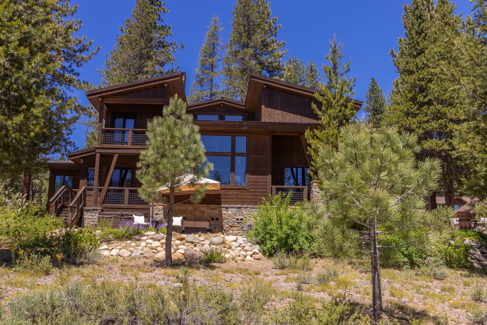 A stunning mountain retreat surrounded by towering pines and natural beauty, featuring contemporary wood-and-stone architecture with expansive windows and multiple decks.