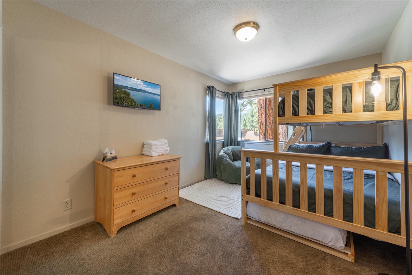 Your cozy retreat features a sturdy wooden bunk bed perfect for family or friends, crisp linens, and ample storage in the dresser. Natural light streams through the window, creating a warm, welcoming space for restful nights.