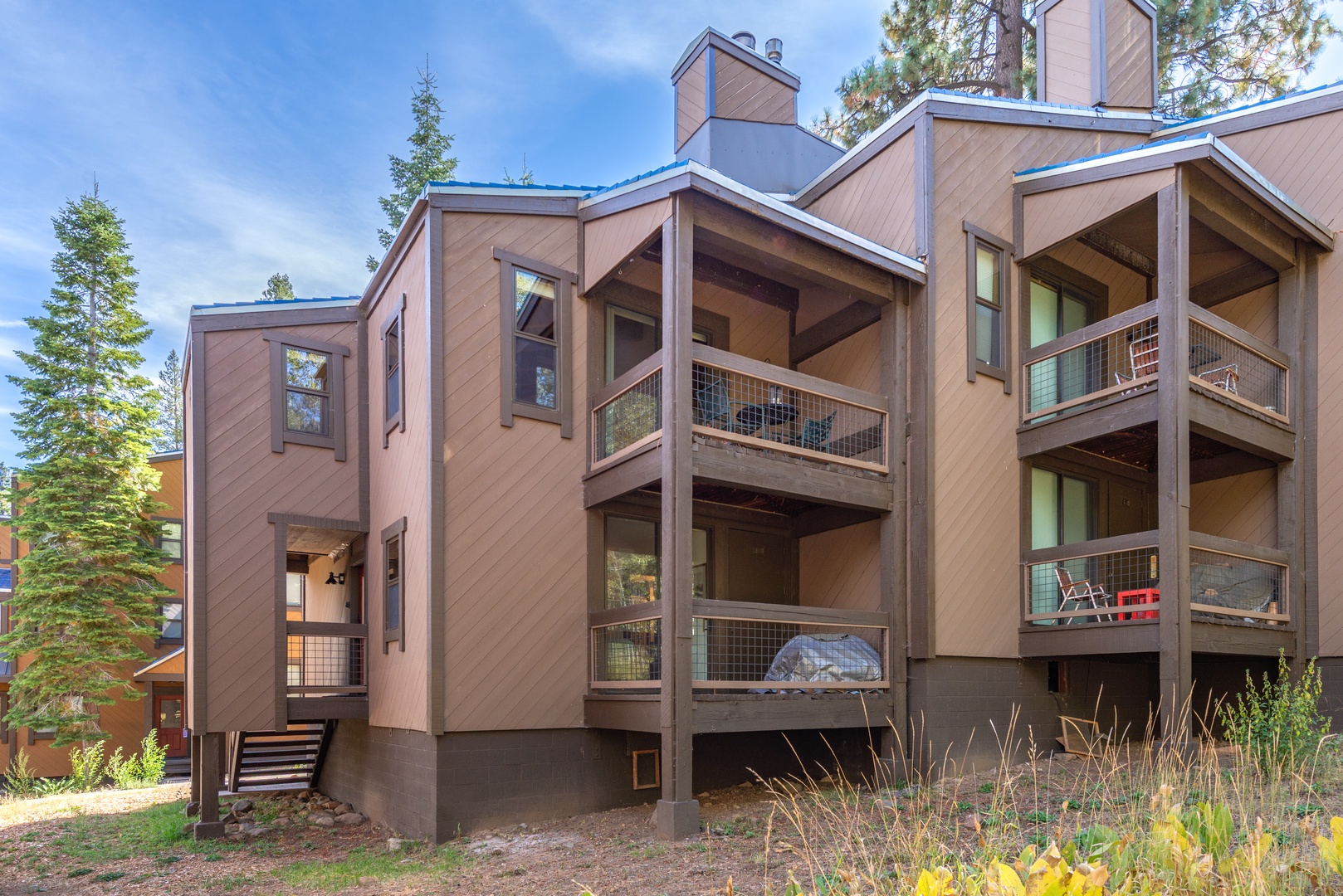 This modern multi-level building nestled among evergreens features spacious balconies with forest views. The contemporary architecture and natural surroundings create a peaceful mountain retreat setting.