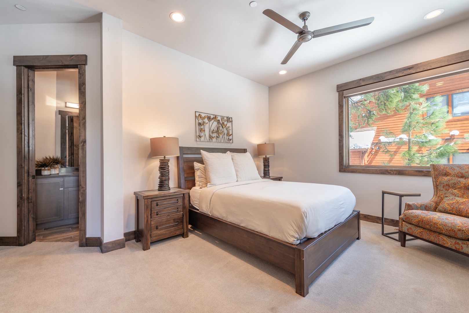 Unwind in your stylish bedroom featuring rich wood furnishings, crisp linens, and peaceful garden views through the large window.