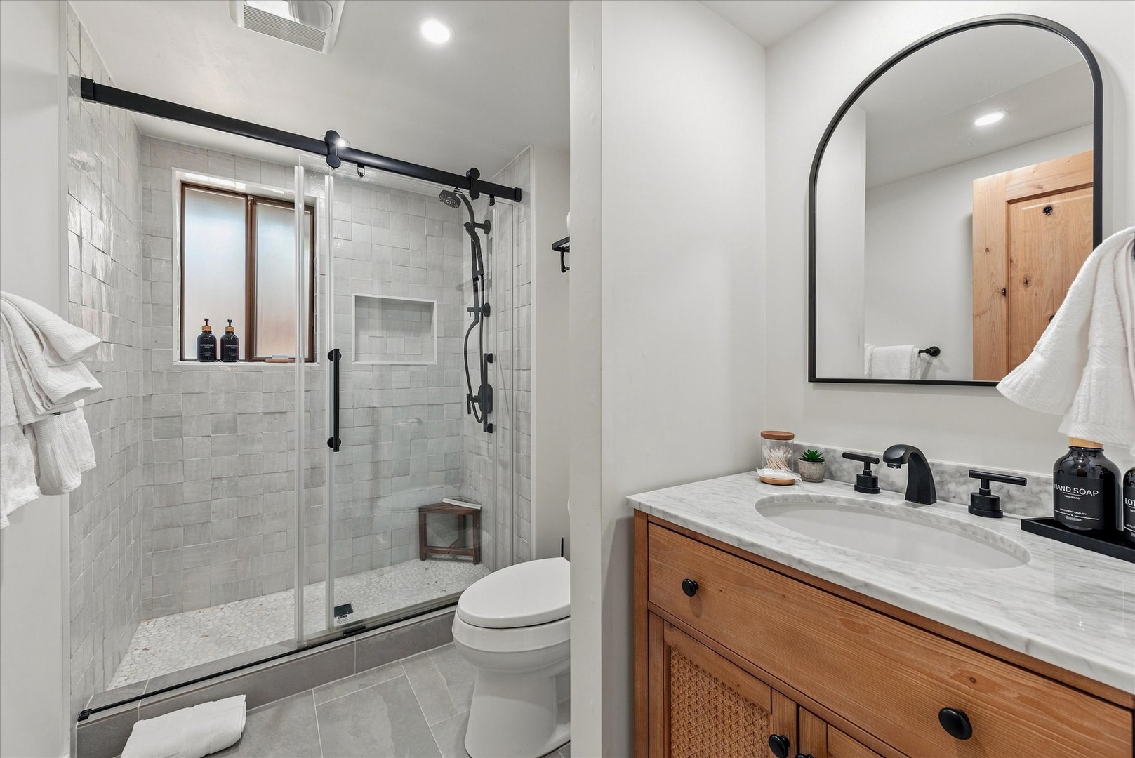 The downstairs bathroom features a walk-in shower with sleek barn-style door. Fresh towels and amenities await your arrival.