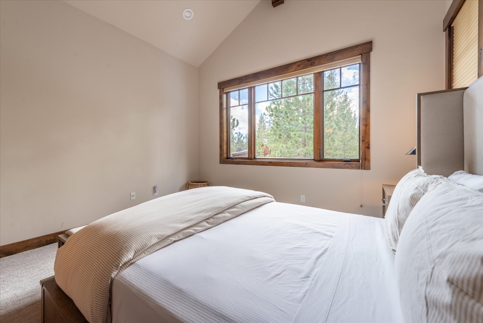 Drift off in this serene bedroom with crisp linens and peaceful forest views through large windows.